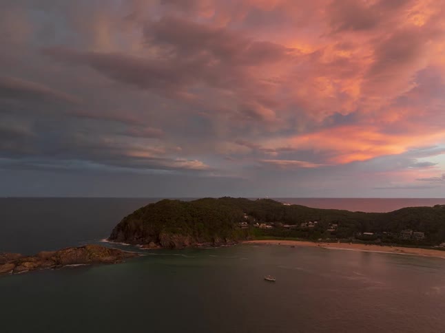 A dramatic timelapse shows vibrant mammatus clouds glowing at sunset and moving over a tranquil coastal bay with a forested headland