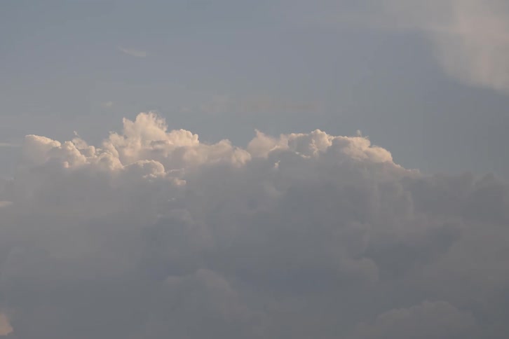 A serene time-lapse captures fluffy white cumulus clouds slowly drifting and changing shape across the sky