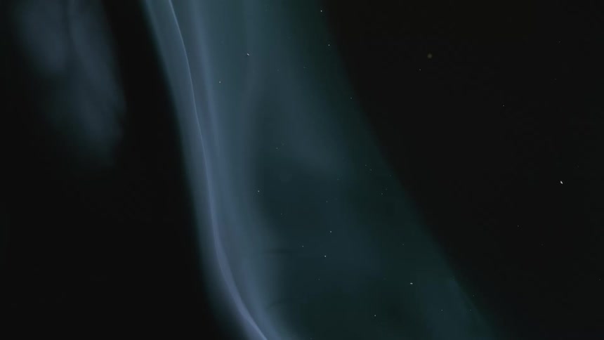 Abstract background of ethereal smoke rising in slow motion against a black background with particles floating in the air