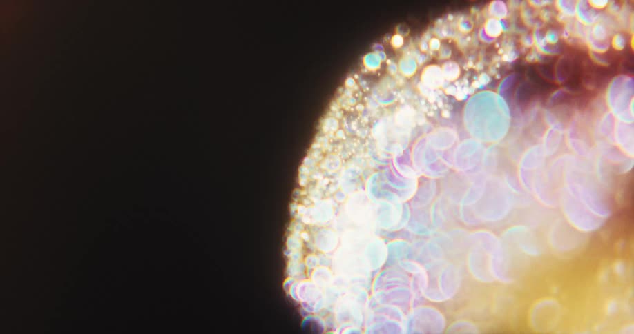A sparkling, orb-like cluster of prismatic lights slowly disperses into a trail of purple bokeh