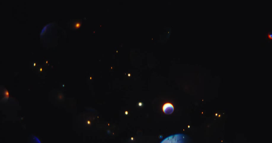 A magical galaxy of colorful, shimmering bokeh orbs and particles floats abstractly in the dark