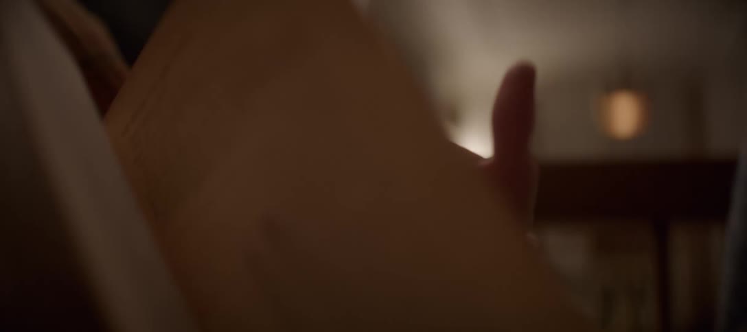 A close-up of a woman's hand turning the page of a book while reading in a cozy, dimly lit room
