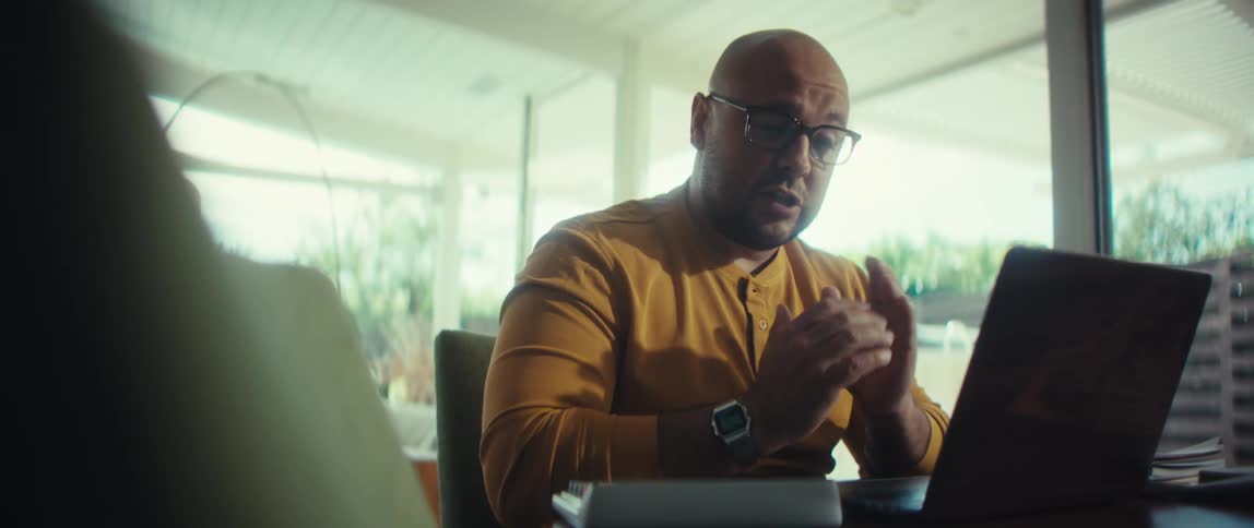 A professional man in glasses actively participates in a video conference from his brightly lit home office