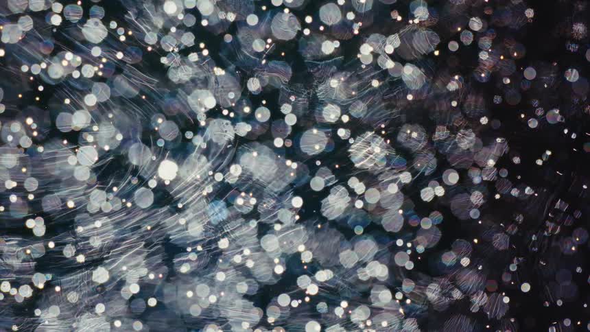 Mesmerizing out-of-focus light particles and bokeh swirl in a cosmic dance against a dark background