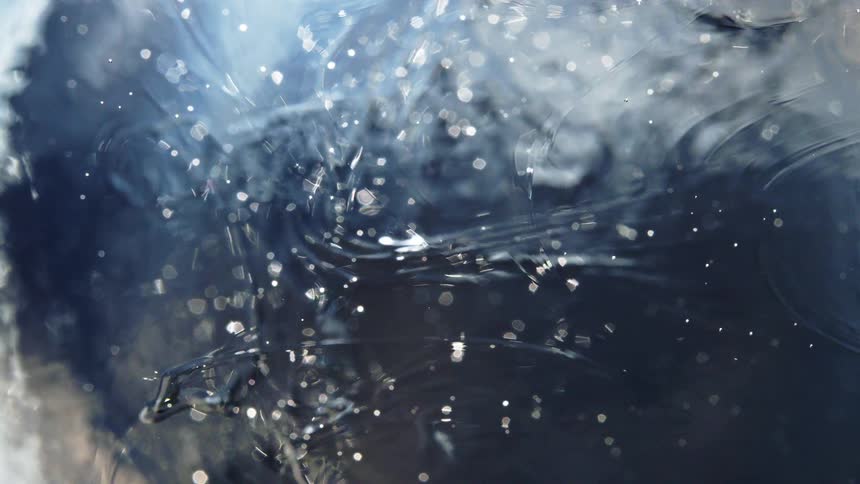 An enchanting abstract macro shot shows shimmering particles suspended and swirling in a dark, mysterious liquid