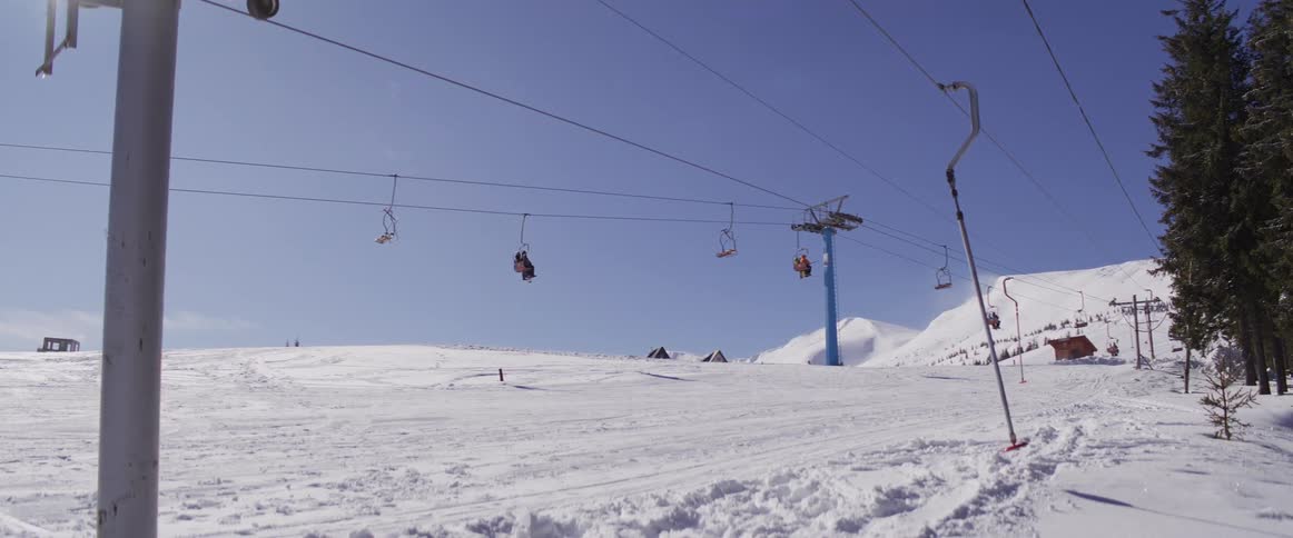 A chairlift and a T-bar lift operate at a snowy mountain ski resort on a bright, sunny day