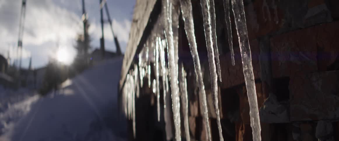 Sunlight glistens off long icicles hanging from a stone wall in a snowy winter landscape