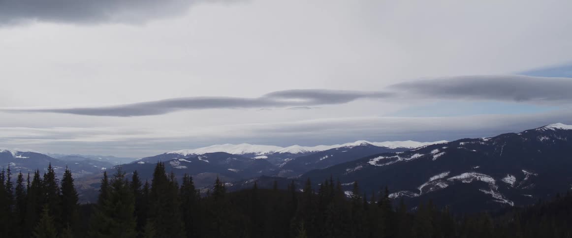 A majestic time-lapse captures unique lenticular clouds gliding over a vast, snow-covered mountain range