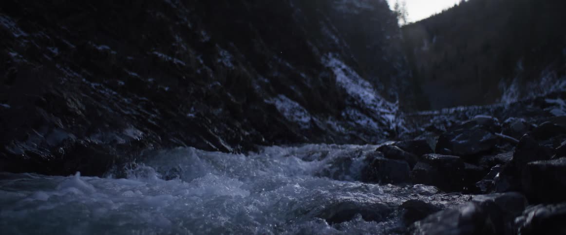 A turbulent mountain river rushes over rocks in a snowy canyon in a dramatic slow-motion close-up