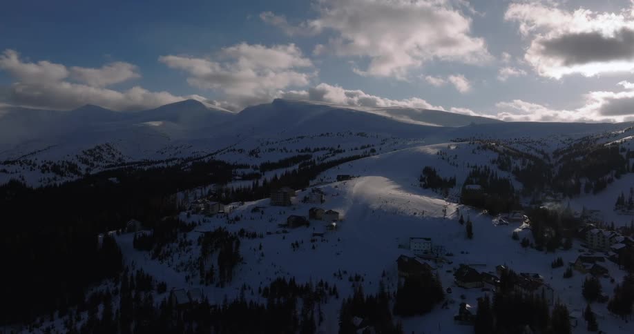 Breathtaking aerial view of a secluded ski resort nestled in the majestic snow-covered mountains under a dramatic cloudy sky