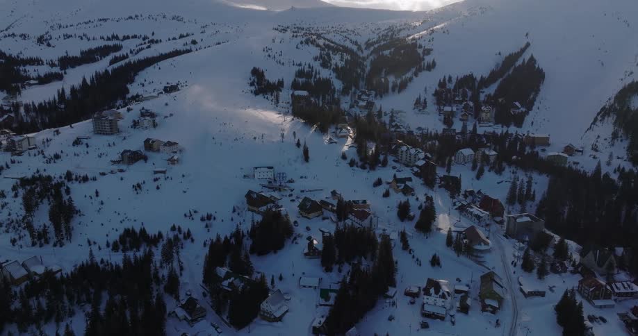 A slow aerial shot reveals a picturesque ski resort village blanketed in snow on a majestic mountain at sunrise
