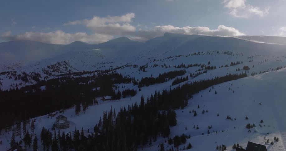 A stunning aerial view flies over a snowy mountain landscape dotted with trees and lodges on a beautiful winter day
