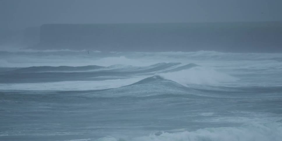 Dramatic slow-motion view of a turbulent sea with powerful waves rolling under a grey, stormy sky