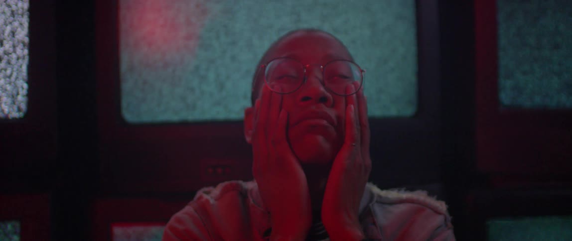 A person wearing glasses holds their face while sitting in front of TV's full of static