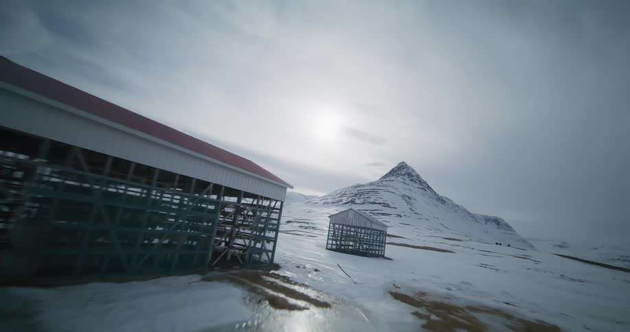 Slowly gliding past traditional fish drying racks across a vast snowy landscape toward the iconic Kirkjufell mountain in Iceland