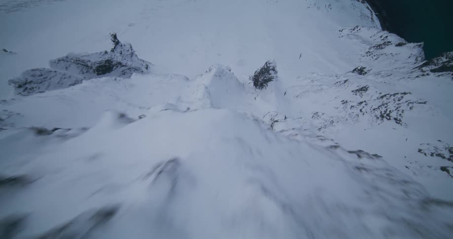 Thrilling FPV drone footage captures a dramatic dive down a steep, snowy mountain slope next to the cold sea