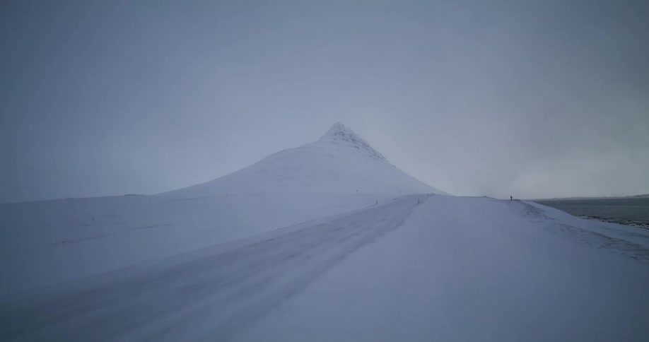 Aerial shot reveals the iconic Kirkjufell mountain and a snow-covered road in a vast, wintry Icelandic landscape