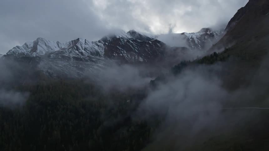 Clouds hover around snowy mountains
