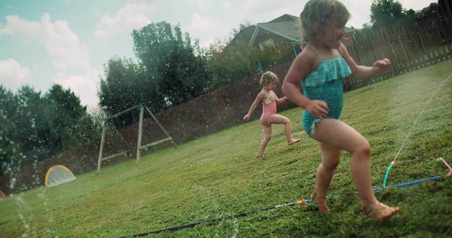 Little girls running through sprinklers on a bright sunny day