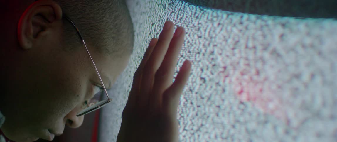 A person in glasses rests their head against a TV playing static