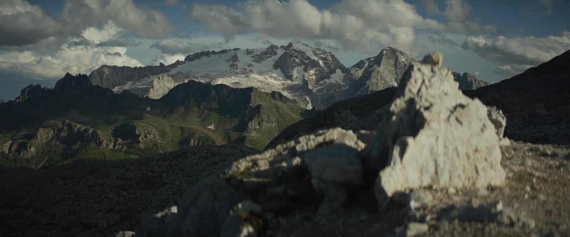 A cinematic slow pan reveals the majestic, snow-capped Marmolada mountain range in the Dolomites under a dramatic, cloudy sky