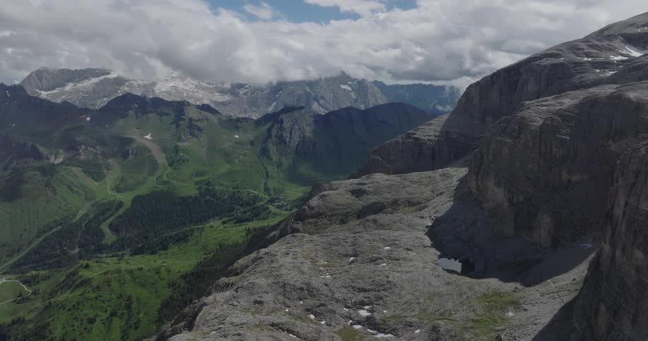 A breathtaking static aerial view of the majestic Dolomite mountains reveals a dramatic landscape of rocky terrain and a lush green valley below