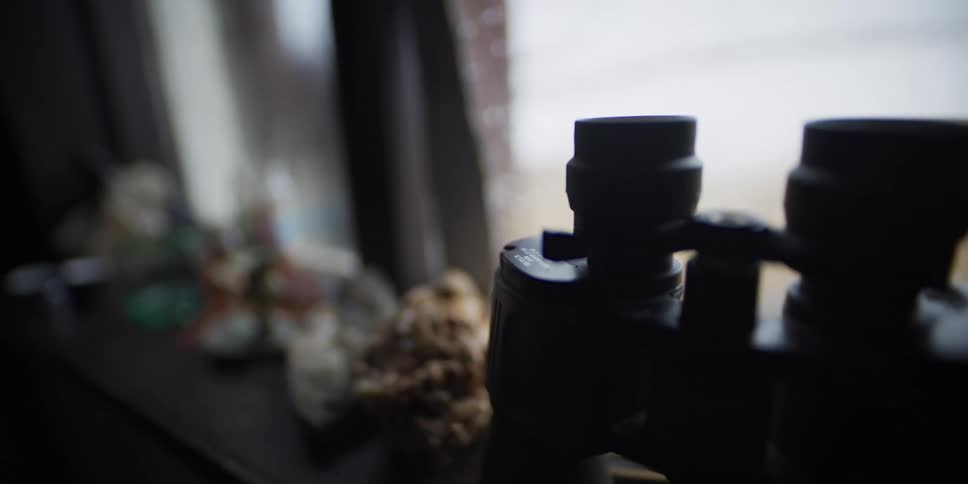 A slow dolly shot reveals a pair of binoculars and collected rocks silhouetted on a windowsill