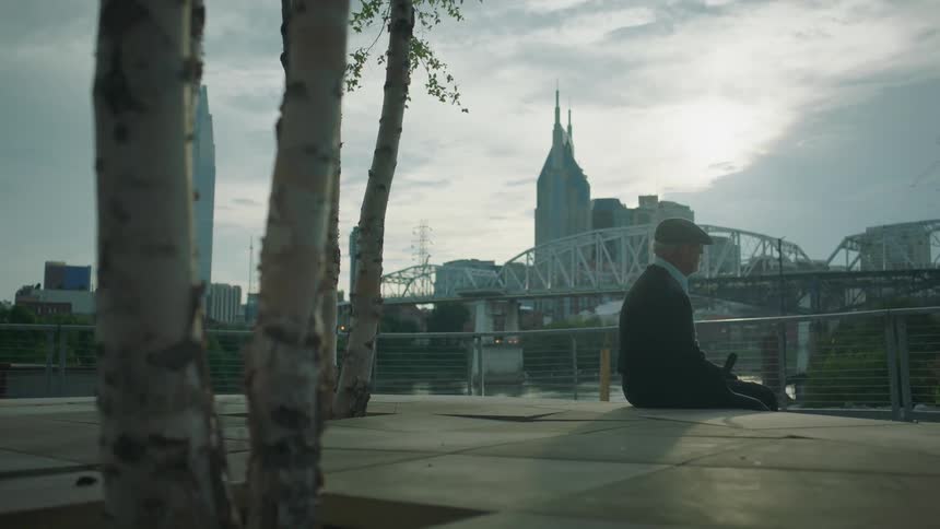 Older man sitting on concrete platform with city in the distance