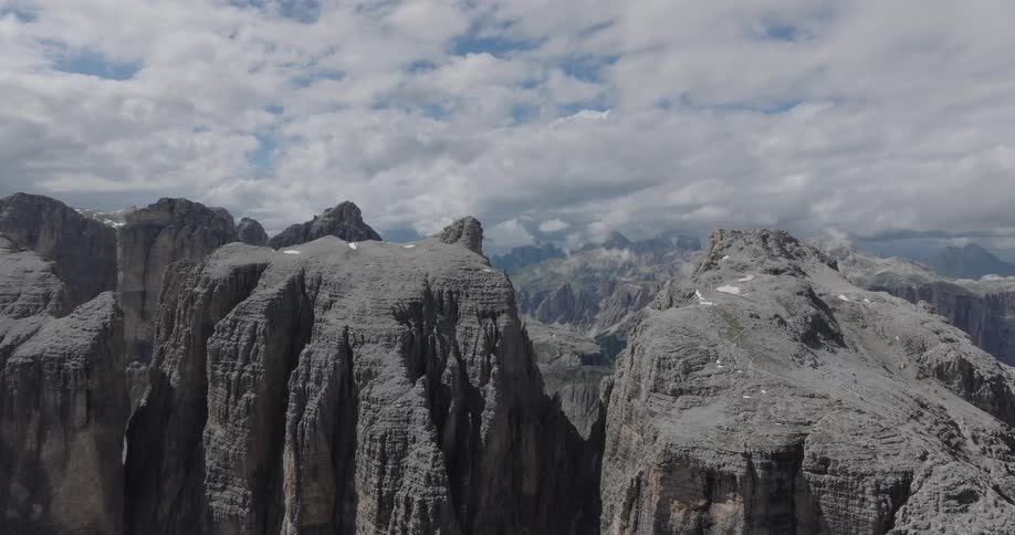 A slow aerial pullback reveals the majestic and rugged peaks of a vast mountain range under a cloudy sky