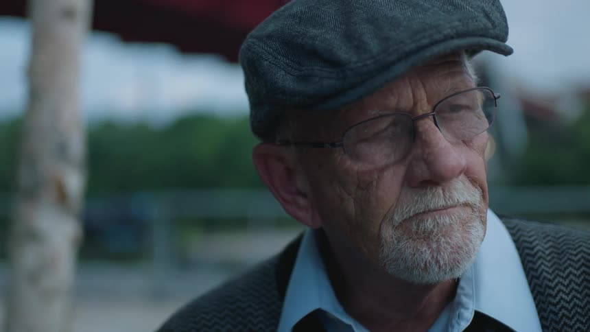 An older man lifts his head and nods slightly