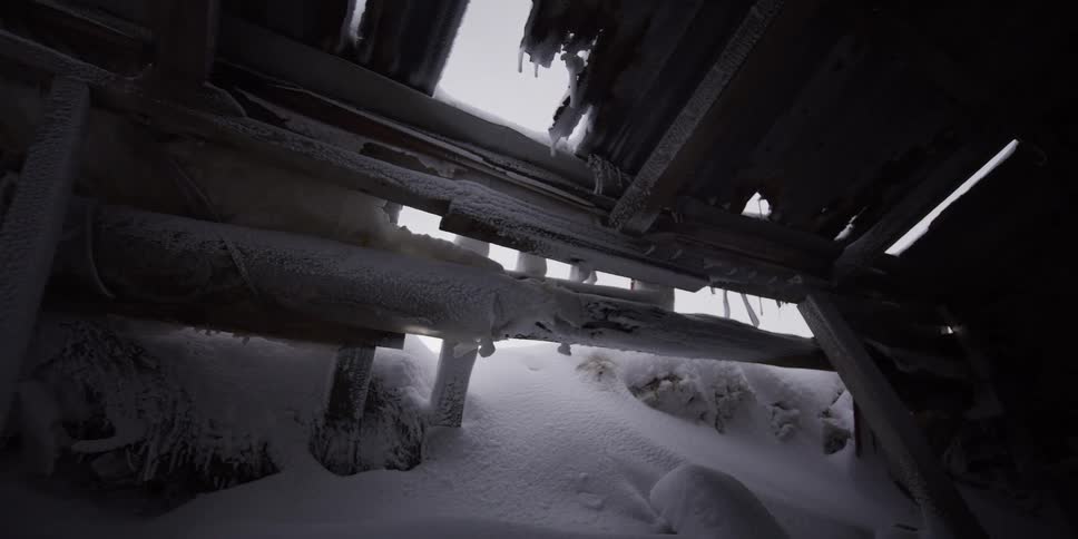 A slow pan reveals the snow-covered and frozen interior of an abandoned, dilapidated shelter in the dead of winter