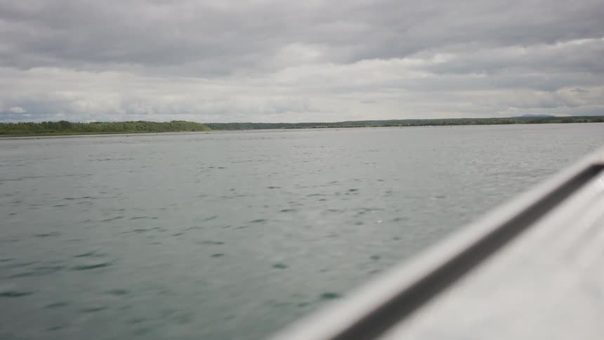A serene view from a boat of a wide, calm lake or river under a cloudy sky