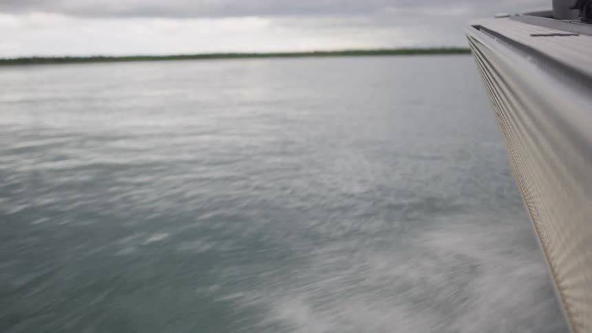 View from the side of a speeding boat as it cuts through the water, creating a wake on a cloudy day