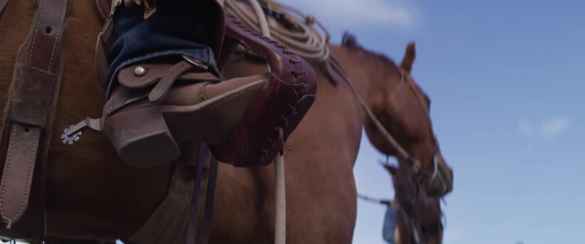 Close-up detail shot of a cowboy's spurred boot resting in a leather stirrup while on horseback