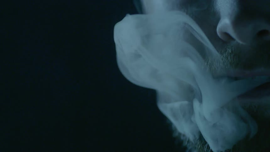 A man slowly blows smoke out of his mouth