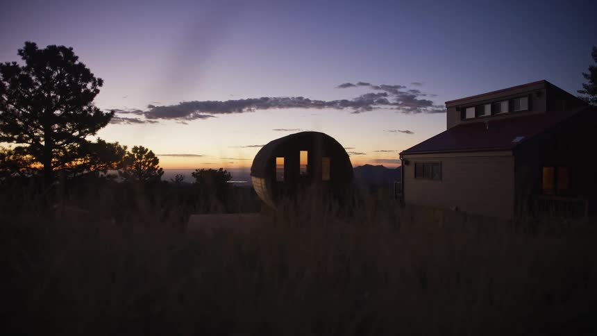 Timelapse of a modern architectural home and a unique pod structure glowing with warm lights against a peaceful twilight sky