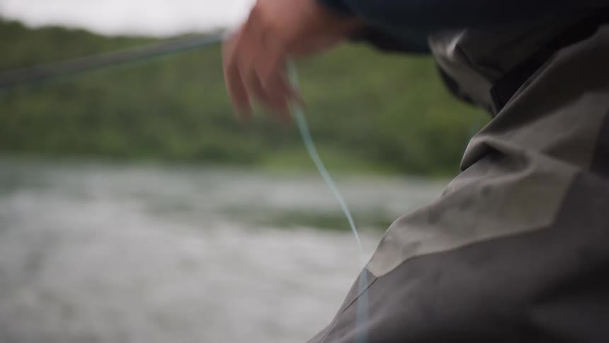 Slow motion close-up of a fly fisherman's hands pulling and releasing the line while casting in a river