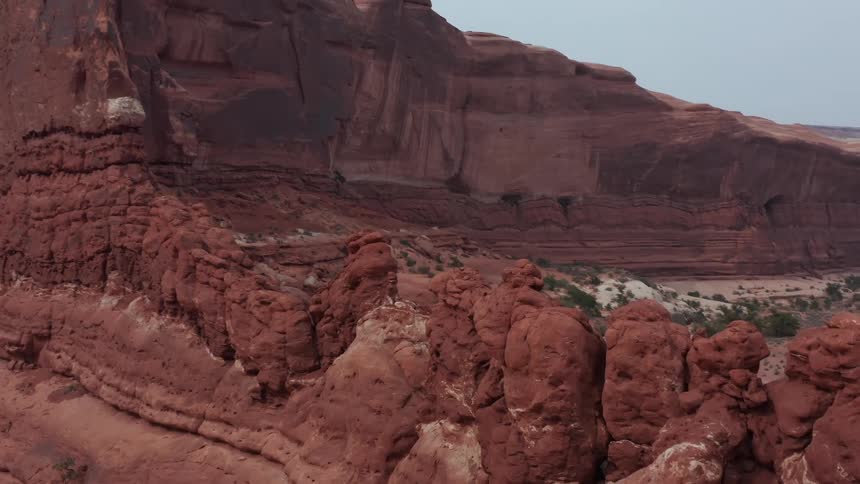 A slow aerial pan reveals the stunning and rugged red rock formations of a vast desert canyon under an overcast sky