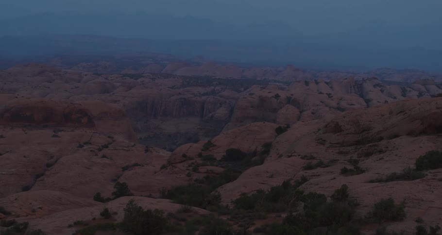 A slow, expansive aerial shot reveals a vast and rugged desert canyon landscape under a hazy twilight sky