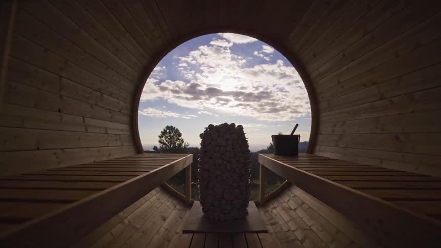 A relaxing slow push-in shot from inside a wooden barrel sauna reveals a stunning view of the sky through a large circular window