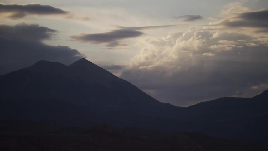 The dark silhouette of a mountain range stands against a majestic sky filled with dramatic, sunlit clouds