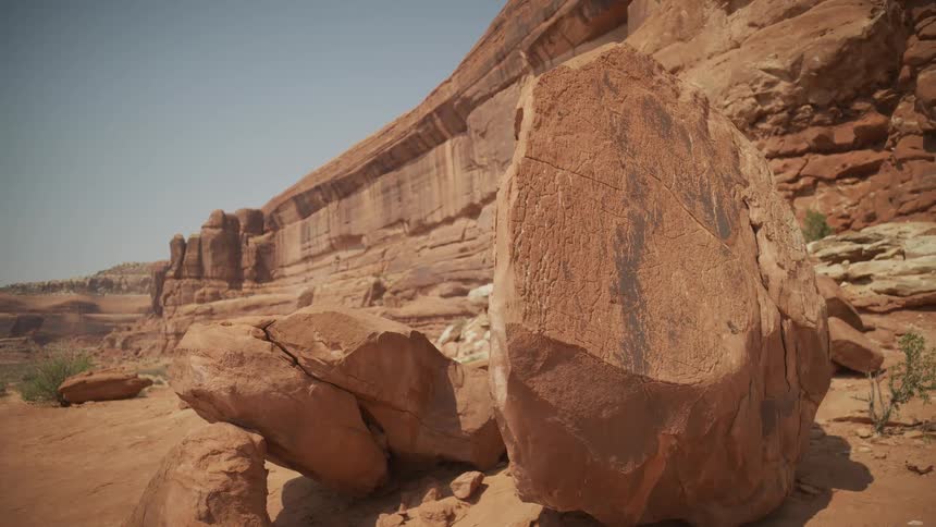 A large boulder with ancient petroglyphs sits in a sun-drenched red rock canyon
