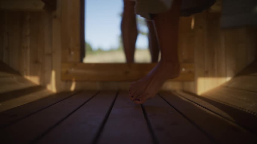Low angle shot of a barefoot couple entering a traditional wooden sauna before the door closes and steam fills the room