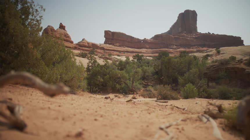 A stunning low-angle, wide shot of a desert landscape featuring prominent red rock formations under a bright, sunny sky