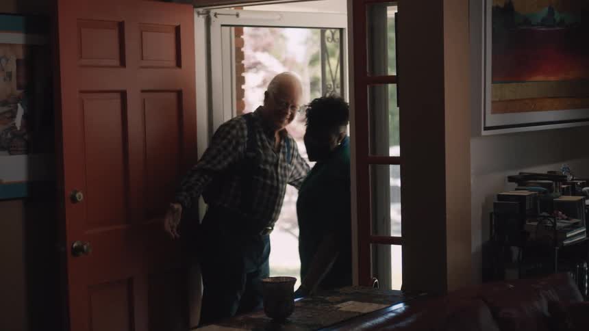 An elderly man warmly greets and hugs his home health aide as she arrives for a visit at his house
