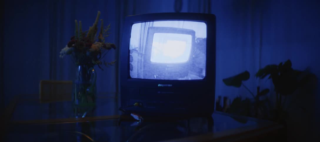 A surreal video feedback loop plays on an old CRT television screen in a dark, blue-lit room