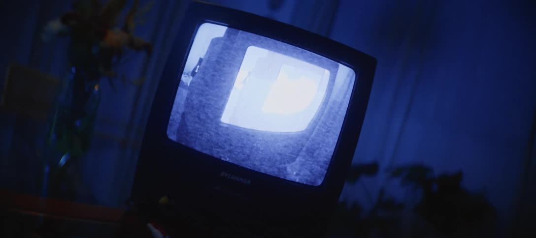 An old CRT television plays a mysterious black and white video in a dark room illuminated by blue light