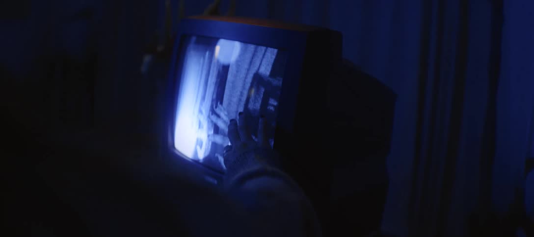 A hand reaches out to touch the glowing, static-filled screen of a retro television in a dark, mysterious room