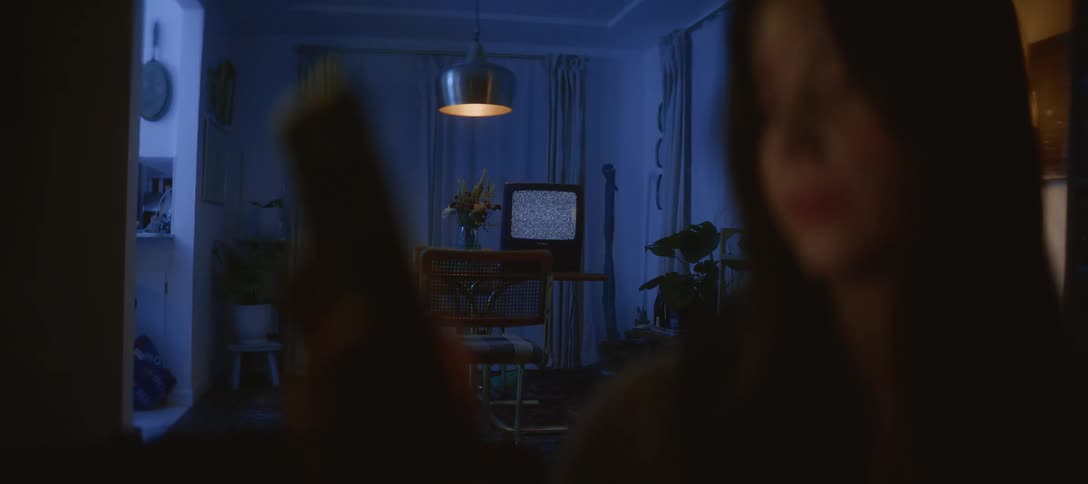 An out-of-focus person is illuminated by their smartphone in a dark blue room as a retro television displays only static