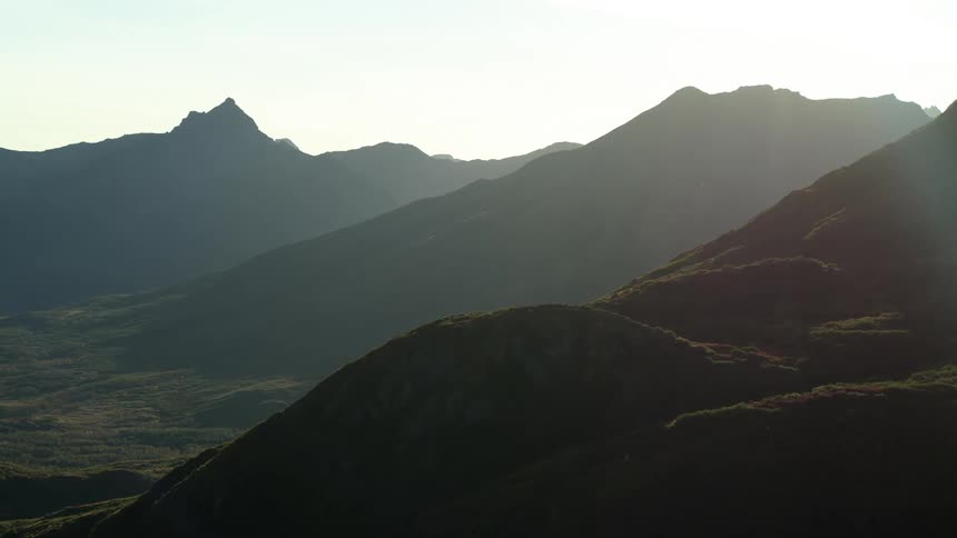 A tranquil, static view of a layered mountain range silhouetted against the bright morning sun